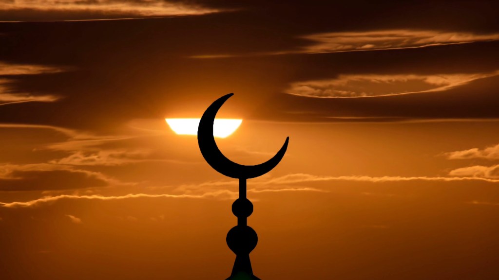 Silhouette of a crescent moon and star against a sunset sky.